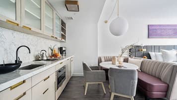 A modern kitchen with a marble countertop, a sink, and a stove. There is a dining area with a round table and chairs.