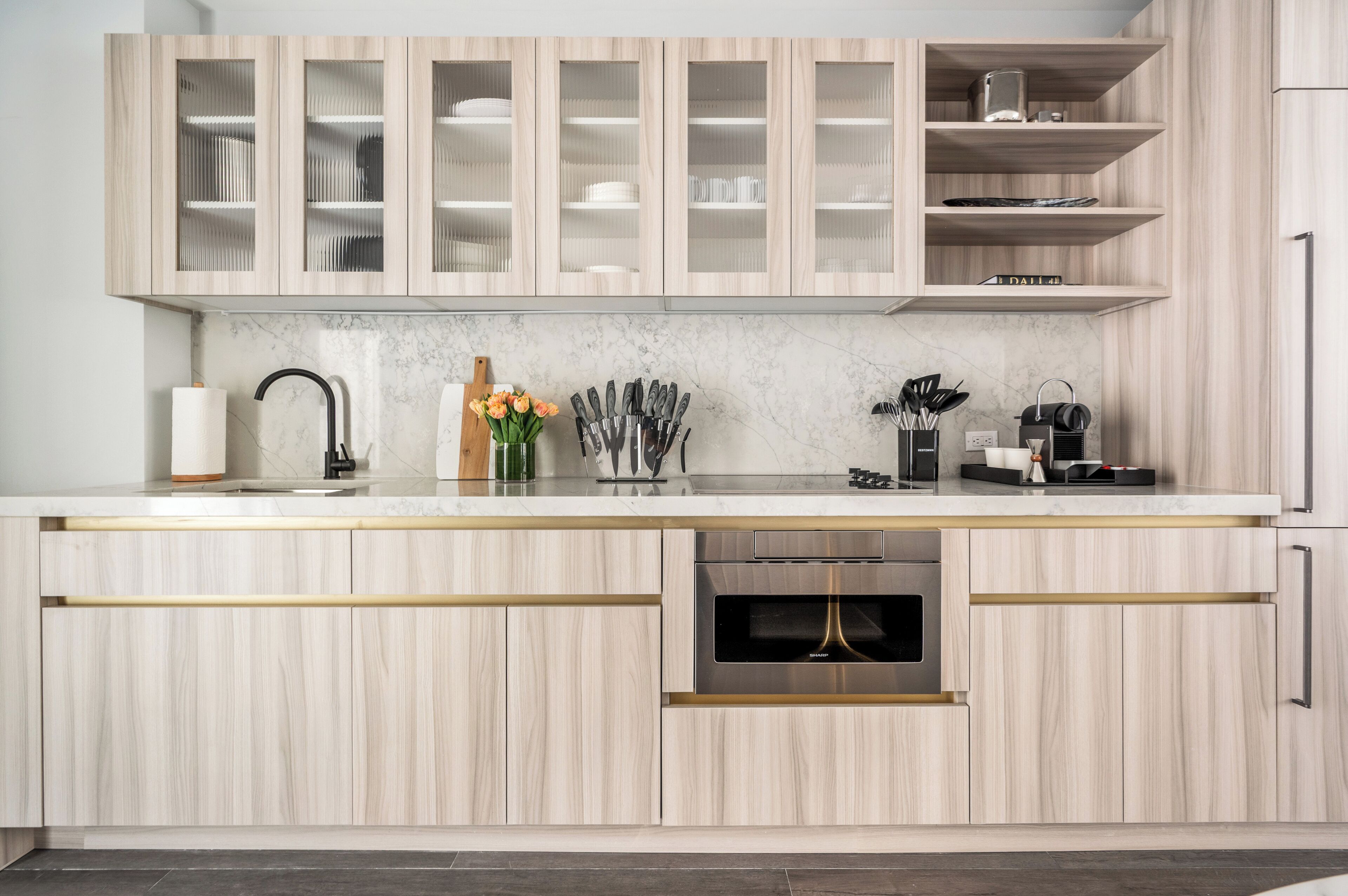 Una cocina moderna con armarios de madera clara, encimera de mármol y electrodomésticos integrados.