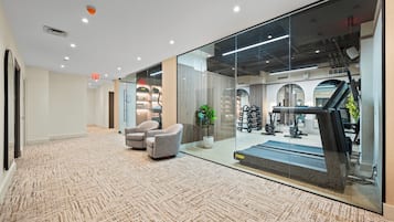 Ein modernes Interieur mit Teppichboden, einer Sitzecke und einer Glaswand, die zu einem Fitnessraum mit Trainingsgeräten führt.