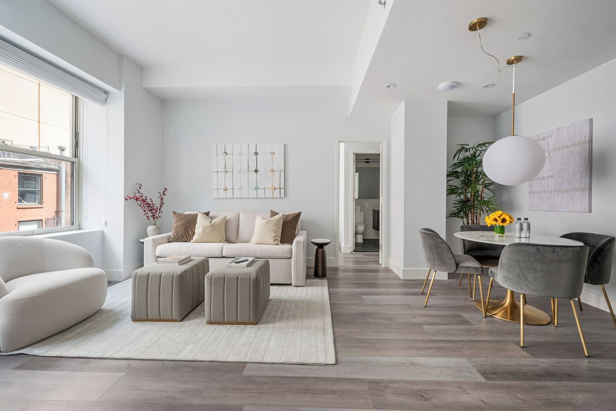 A modern living room with a sofa, ottoman, and dining area with chairs and a table.