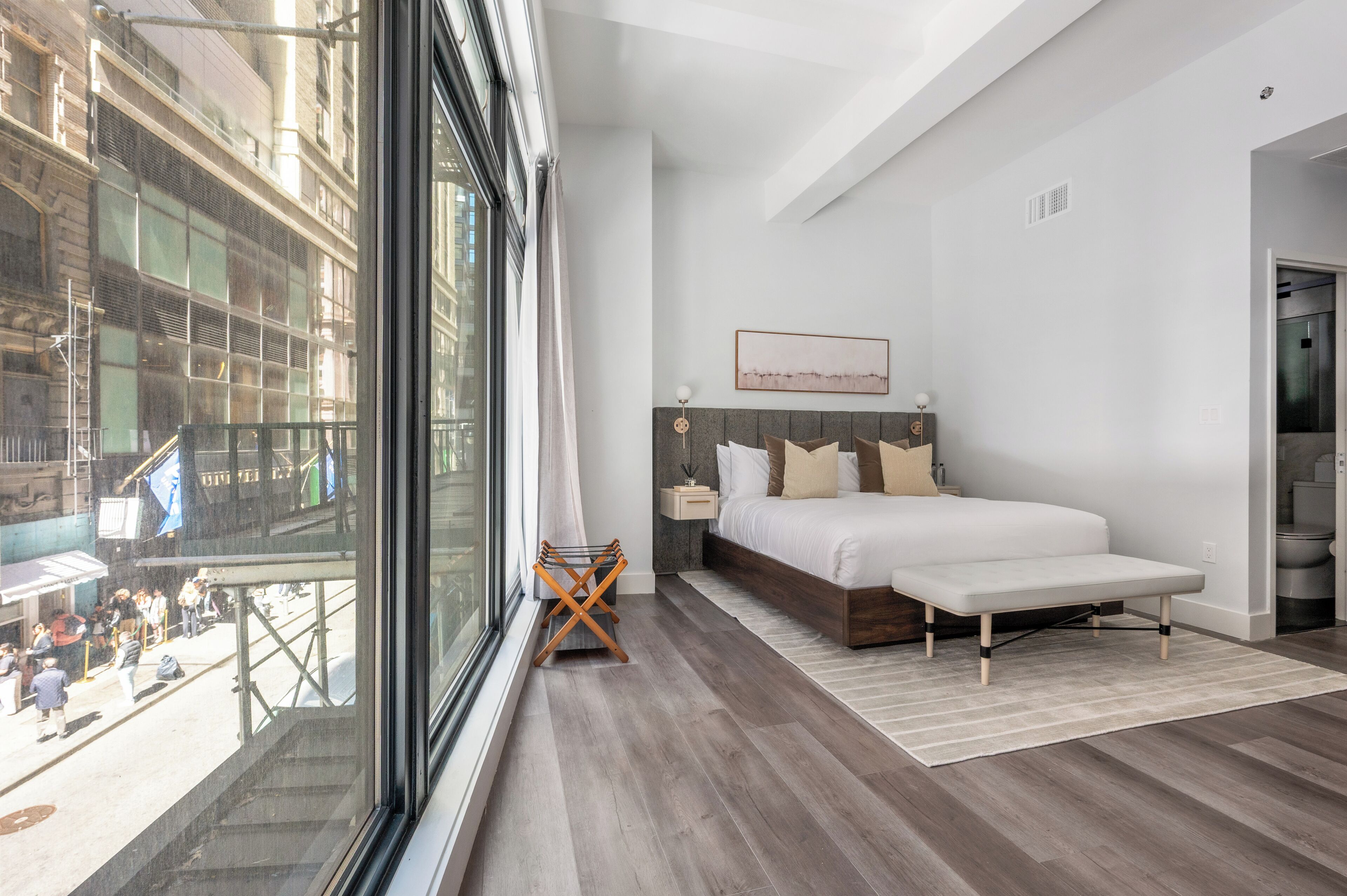 Un dormitorio moderno con un ventanal grande, una cama, una mesita de noche y vistas a la ciudad.