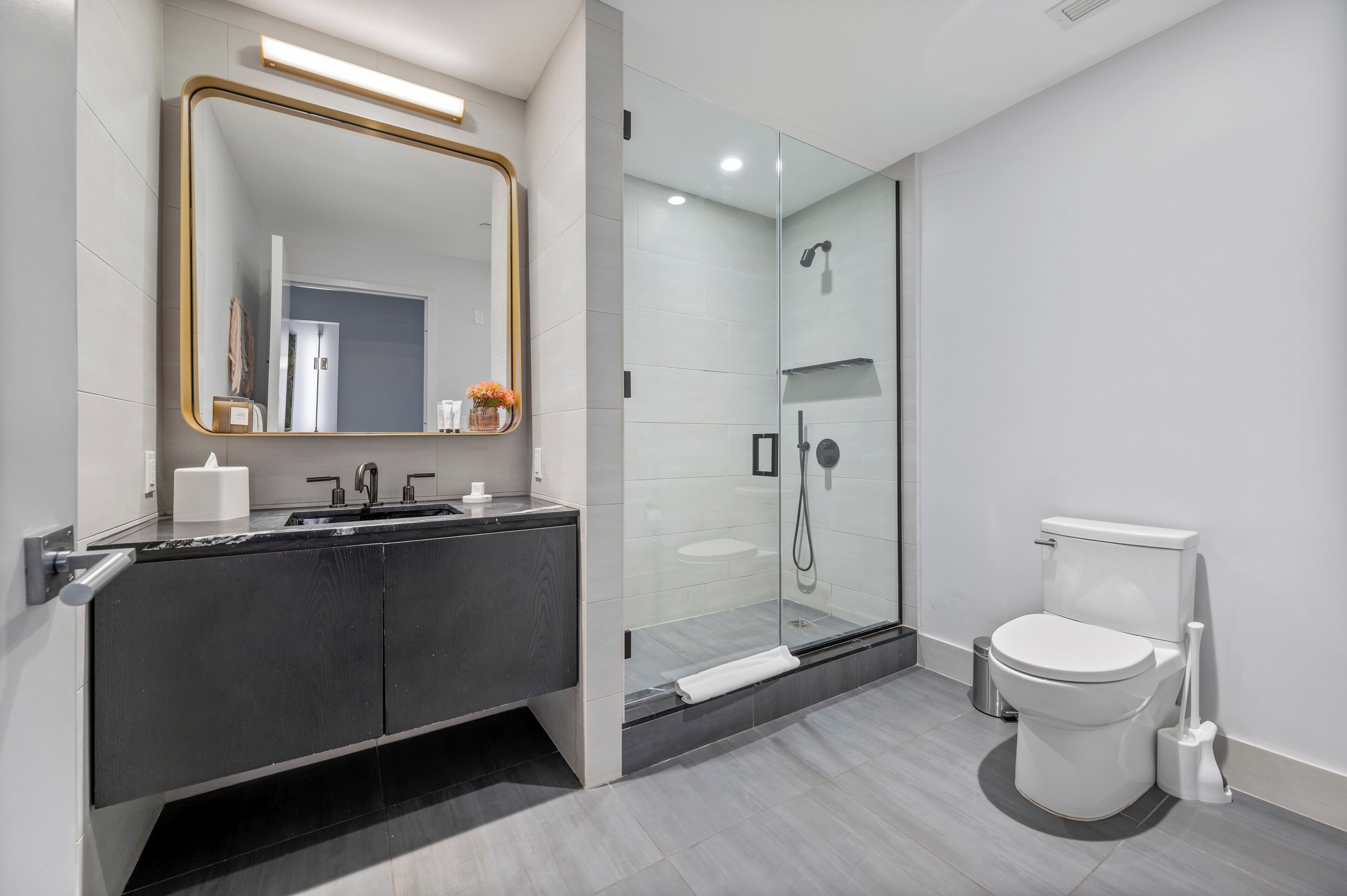 A modern bathroom with a glass-enclosed shower, a vanity with a mirror, and a toilet.