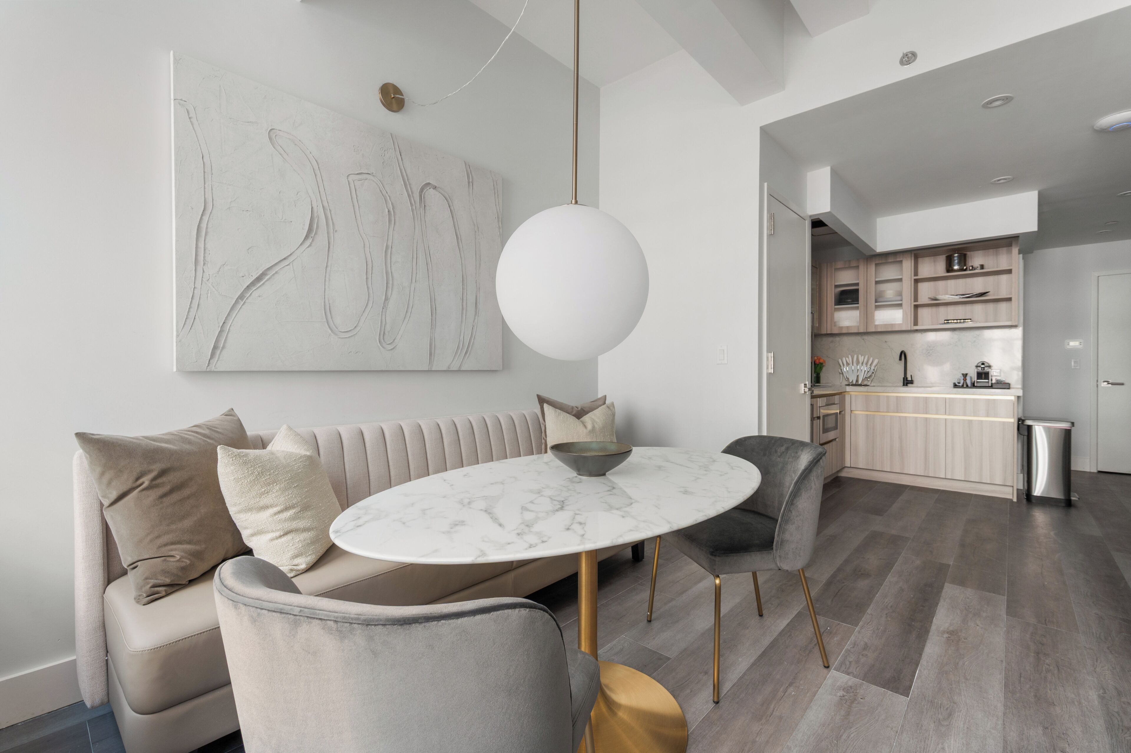 A modern living room with a marble table, grey sofas, and a minimalist kitchen in the background.