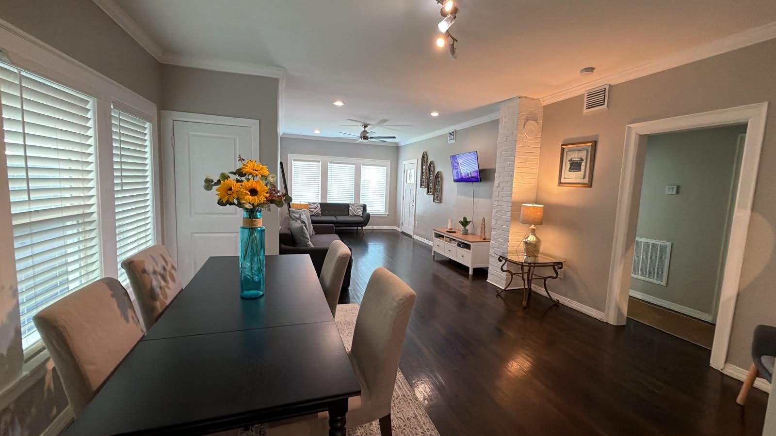 A dining area with a black table and chairs, a vase with flowers, and a television in the background.