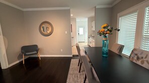A dining area with a dark wood floor, a round mirror on the wall, a table with chairs, and a vase with flowers. - Museum District - Beautiful 2 Br/2Ba with King bed! (Houston)