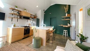 A modern kitchen with wooden cabinets, a central island, and a dining area with stools. - Walkable Modern Retreat (Portland)