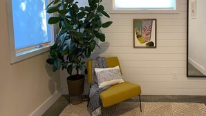 A room with a large potted plant, a yellow armchair with a patterned throw, a framed artwork, and a window with blinds. - Walkable Modern Retreat (Portland)