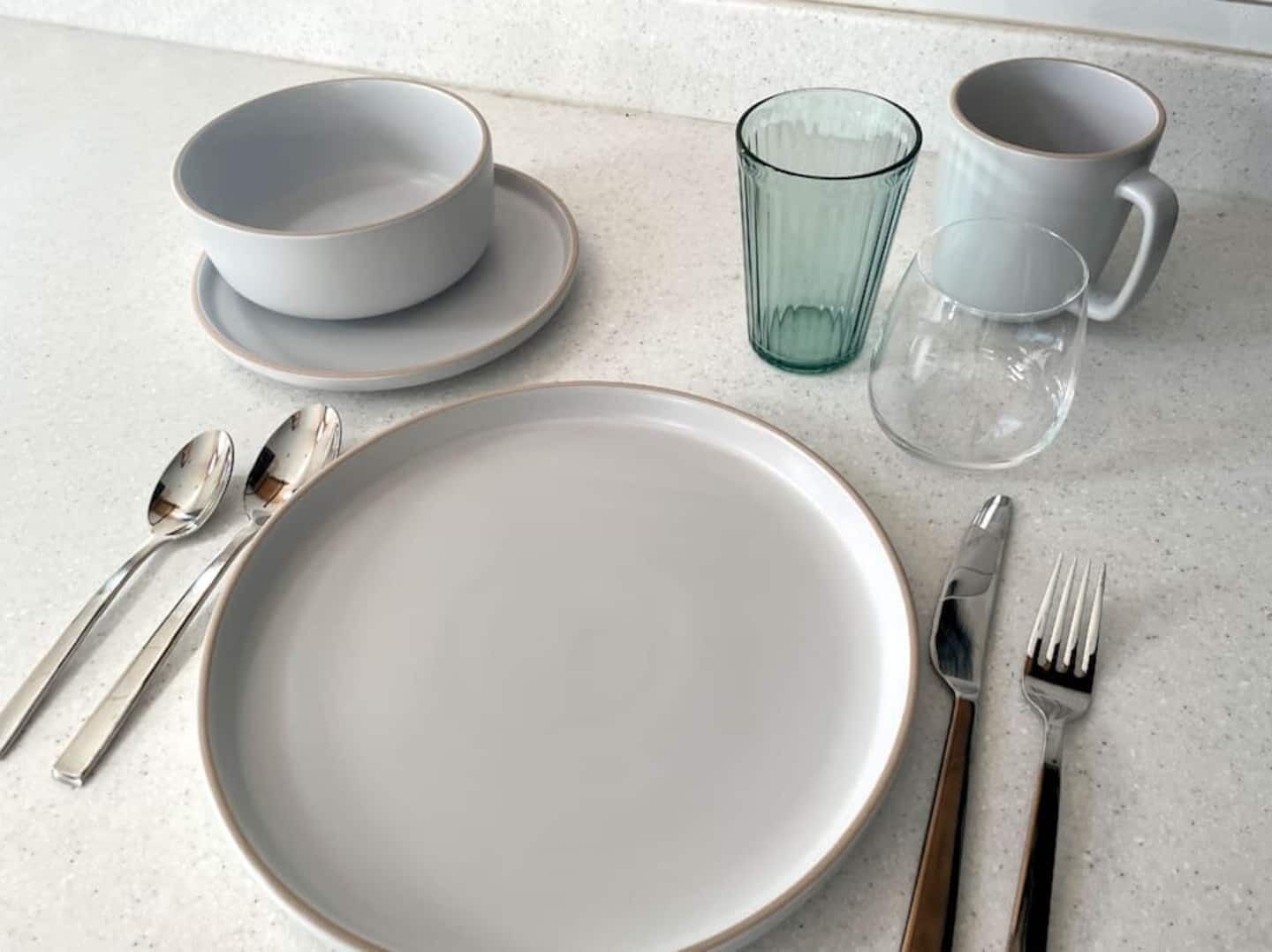 A table set with a white plate, two bowls, a glass, a cup, a fork, and two spoons.