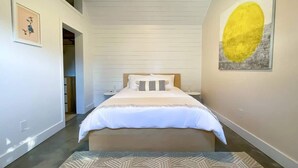 A bedroom with a large bed, a nightstand, a wall-mounted artwork, and a hallway leading to another room. - Walkable Modern Retreat (Portland)