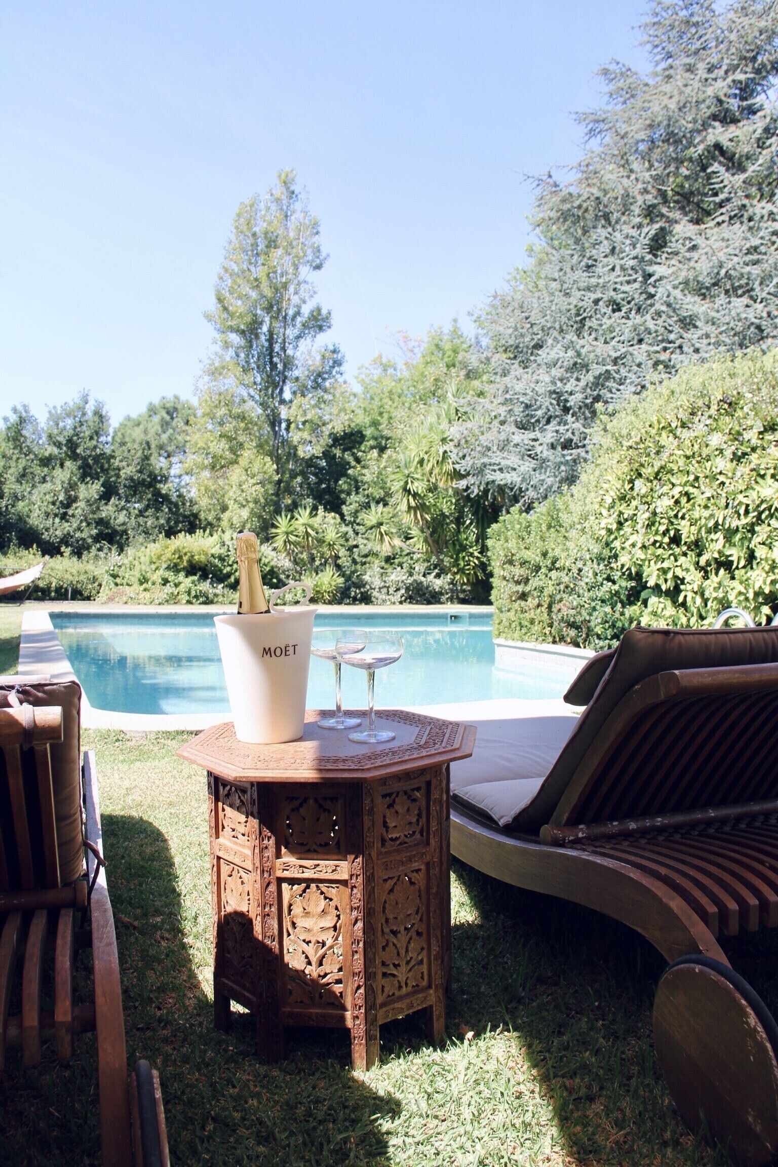 Un área junto a la piscina con una silla de madera, una mesita y una botella de champán Moët.