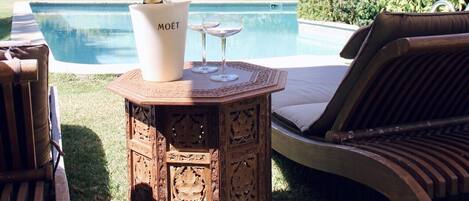 Un área junto a la piscina con una silla de madera, una mesita y una botella de champán Moët.