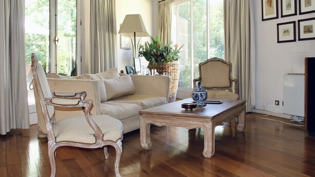 A living room with a sofa, armchair, and coffee table, a lamp, a potted plant, and framed pictures on the wall.