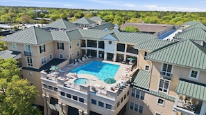 A multi-story hotel with a central swimming pool, outdoor seating, and a view of the surrounding area.