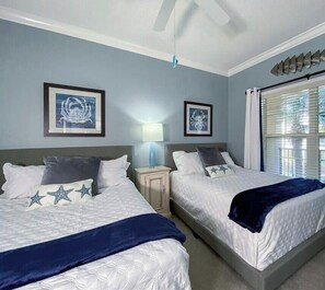 A hotel room with two beds, a nightstand with a lamp, and framed artwork on the walls.
