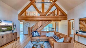 A spacious living room with a wooden staircase, a leather sofa, and a coffee table. - Lincoln Log Cabin, Tranquility close to Downtown (Flagstaff)