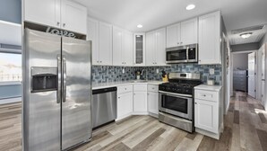 A modern kitchen with white cabinets, stainless steel appliances, a tiled backsplash, and a wooden floor.