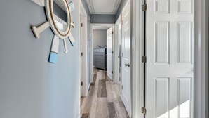 A hallway with a wooden floor, a white door on the right, and a decorative wall piece.