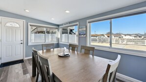 A dining area with a wooden table and chairs, large windows with a view of the beach, and a sign on the wall.