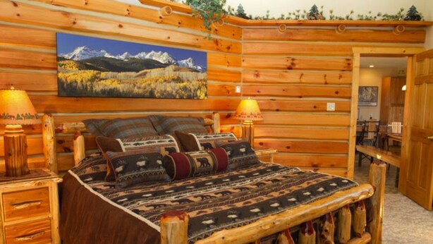 A log cabin-style bedroom with a wooden bed, two bedside lamps, and a painting of a mountain landscape. - Rustic Luxury in the Northwoods l (Ironwood)