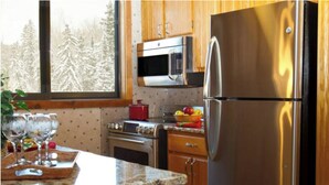 A kitchen with wooden cabinets, a stainless steel refrigerator, a microwave, an oven, and a granite countertop. - Rustic Luxury in the Northwoods l (Ironwood)