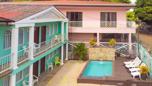 Un edificio de dos pisos con piscina, mobiliario exterior y una pequeña cascada.