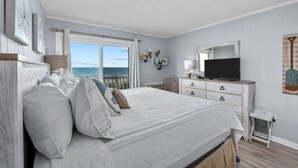 A bedroom with a large bed, a dresser, a television, and a view of the ocean. - 2/2 Oceanfront Condo w/ Pool - Windy Hill (North Myrtle Beach)