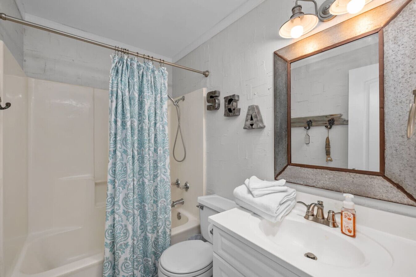 A bathroom with a shower, toilet, sink, and a mirror.