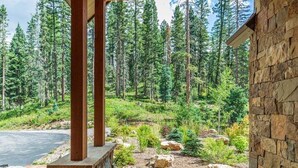 Un bâtiment en pierre surmonté d’une pergola en bois, qui donne sur une zone boisée.