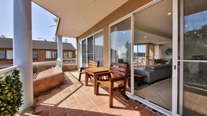 Un patio techado con mesa y sillas, grandes puertas correderas de vidrio y vista a un área residencial.