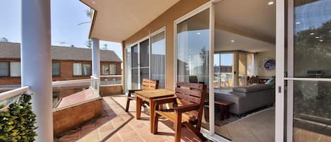 A covered patio with a table and chairs, large sliding glass doors, and a view of a residential area.