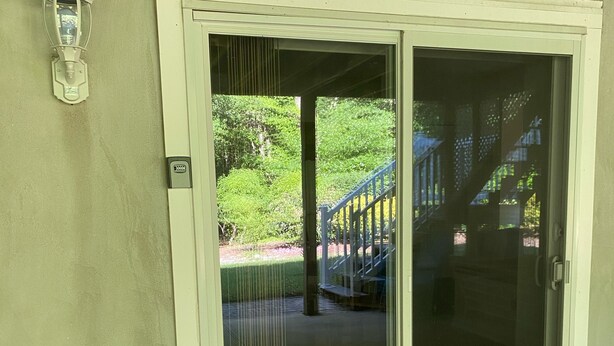 Une porte-fenêtre coulissante donnant sur un espace extérieur agrémenté d’un escalier extérieur couvert et de verdure.