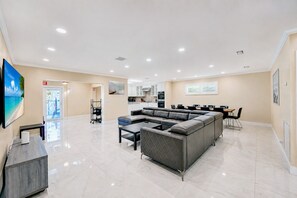 A spacious living area with a sectional sofa, a dining table with chairs, and a kitchen in the background.