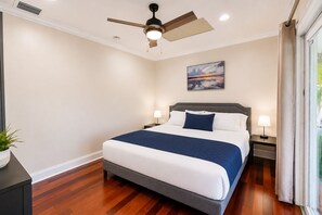 Ein Schlafzimmer mit Bett, Nachttischen, Deckenventilator, einem Gemälde und einem Fenster mit Vorhängen.
