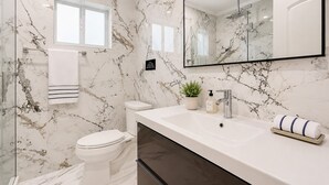 A bathroom with a marble wall, a toilet, a sink with a mirror, and a shower. - Premium Luxury  5BR/4BA Villa near Hollywood Beach (Hollywood)
