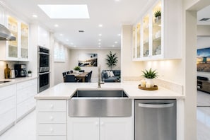 A modern kitchen with white cabinetry, a central island, and a dining area with a table and chairs. - Premium Luxury  5BR/4BA Villa near Hollywood Beach (Hollywood)