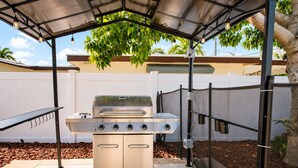 A stainless steel grill with four burners, a side shelf, and a control panel, set up under a metal canopy in a backyard. - Premium Luxury  5BR/4BA Villa near Hollywood Beach (Hollywood)