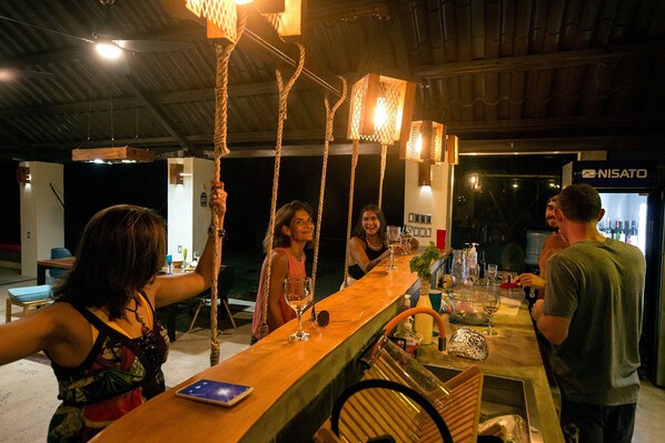 Una zona de bar con mostrador de madera, luces colgantes y dispensador de agua.