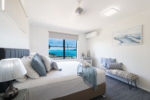 A bedroom with a bed, bedside table, lamp, and a large window with a view. - Airlie Blue On Blue (Airlie Beach)