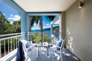 A balcony with a table and chairs, overlooking a scenic view of the sea and greenery. - Resort-style Coastal Charm at Airlie Beach (Airlie Beach)