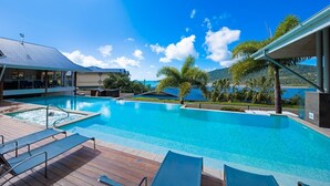 Una piscina con lettini e solarium, circondata da palme e vista sul mare.