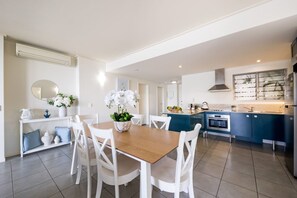 Eine moderne Küche mit weißen Schränken, einer blauen Kücheninsel und einem Essbereich mit Holztisch und weißen Stühlen.