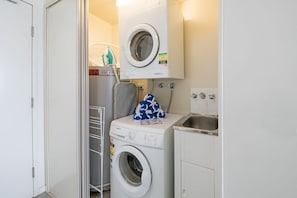 A laundry area with two washing machines, a drying rack, and a sink. - Coastal Charm On Airlie (Airlie Beach)