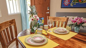 A dining table set with plates, bowls, and a glass. There are chairs around the table, and a vase with flowers is on the table. - Cococabana4 newly renovated 1BR/1BA apar in downtown Coco, 5 min walk to beach. (Playas del Coco)