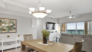 Ett rymligt vardagsrum med ett matbord i trä, en soffa och ett stort fönster med utsikt över havet.