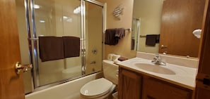 Une salle de bain avec une douche à parois de verre, des toilettes blanches, un lavabo avec un miroir et des meubles en bois.