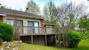 A two-story house with a red door, a balcony, and a stone foundation. - On the Island!  Three bedroom, two bath home. (Holiday Island)
