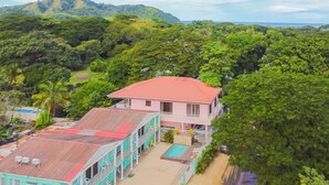 A two-story building with a red roof, surrounded by dense greenery and a view of the ocean. - Cococabana6 newly renovated 1BR/1BA apar in downtown Coco, 5 min walk to beach. (Playas del Coco)