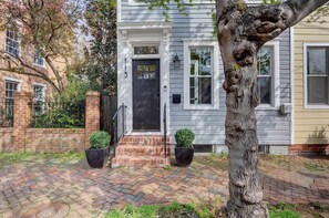 A brick-paved front yard with a house number 113, a black door, and two potted plants.