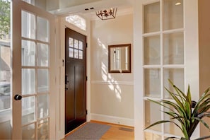 A hallway with a dark door, a mirror on the wall, and a potted plant.