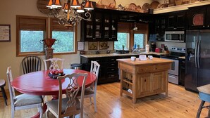 A modern kitchen with dark cabinets, a central island, and a dining area with a red table and white chairs. - Casa Cortina: Eclectic Highlands Retreat w/ Covered Deck | 4 Min to Main Street (Highlands)